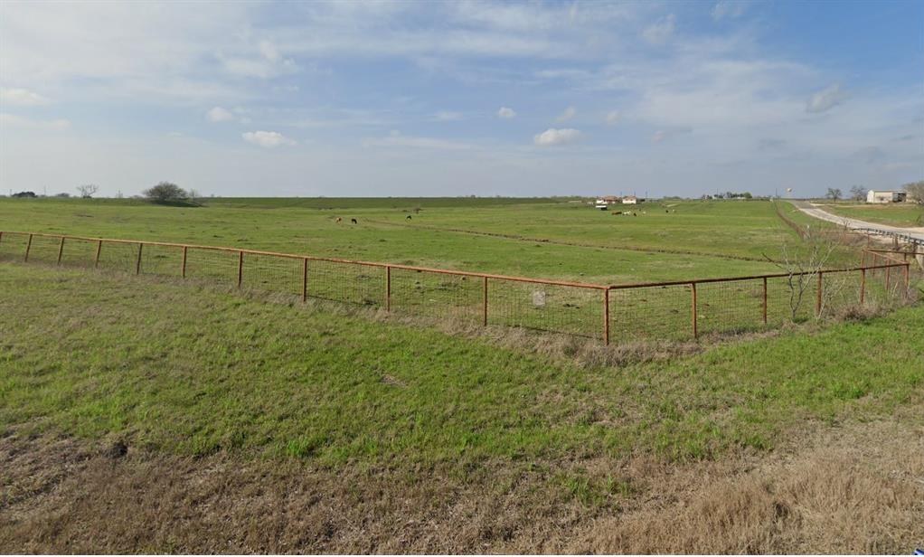 Open pasture behind a rust-colored pipe fence, with cattle grazing in the distance.