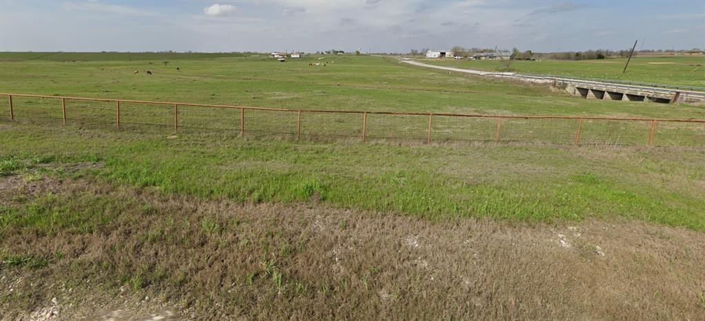 Pasture and fence beside the county road, with a culvert structure in the distance.